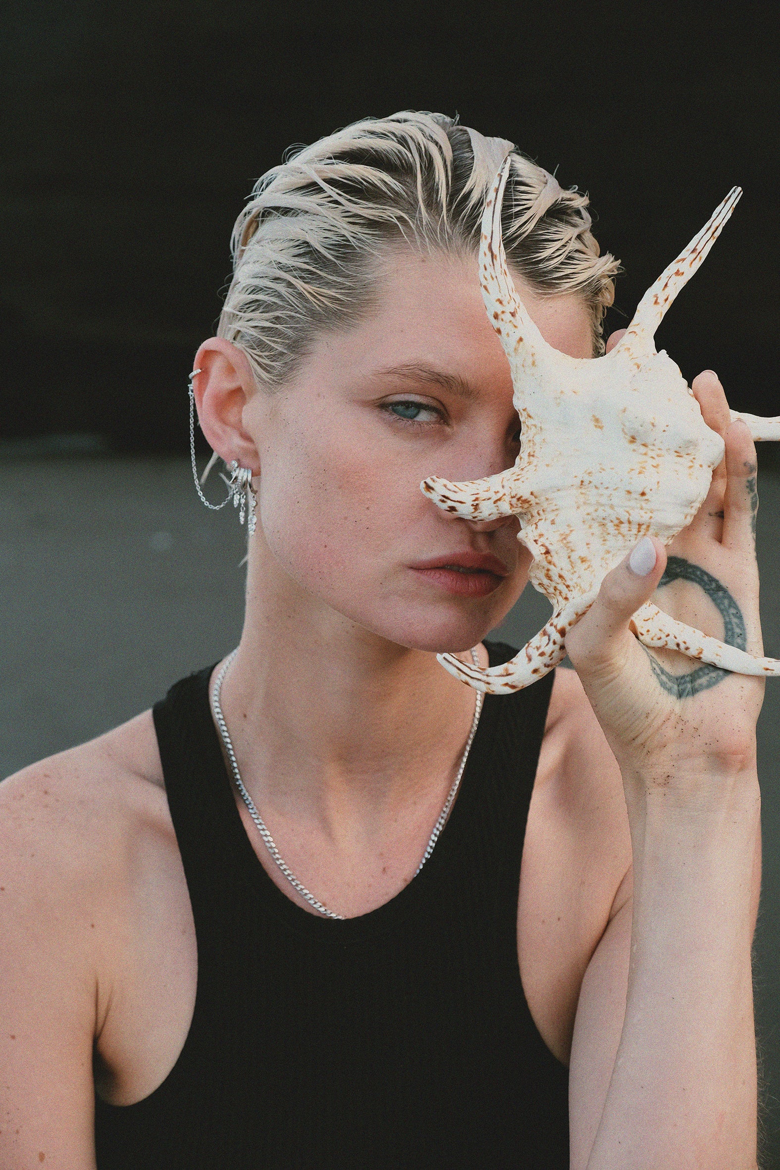 Stylish woman holding a seashell, wearing silver jewelry.