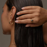 Woman wearing gold earring and ring with a triangular brown gemstone.