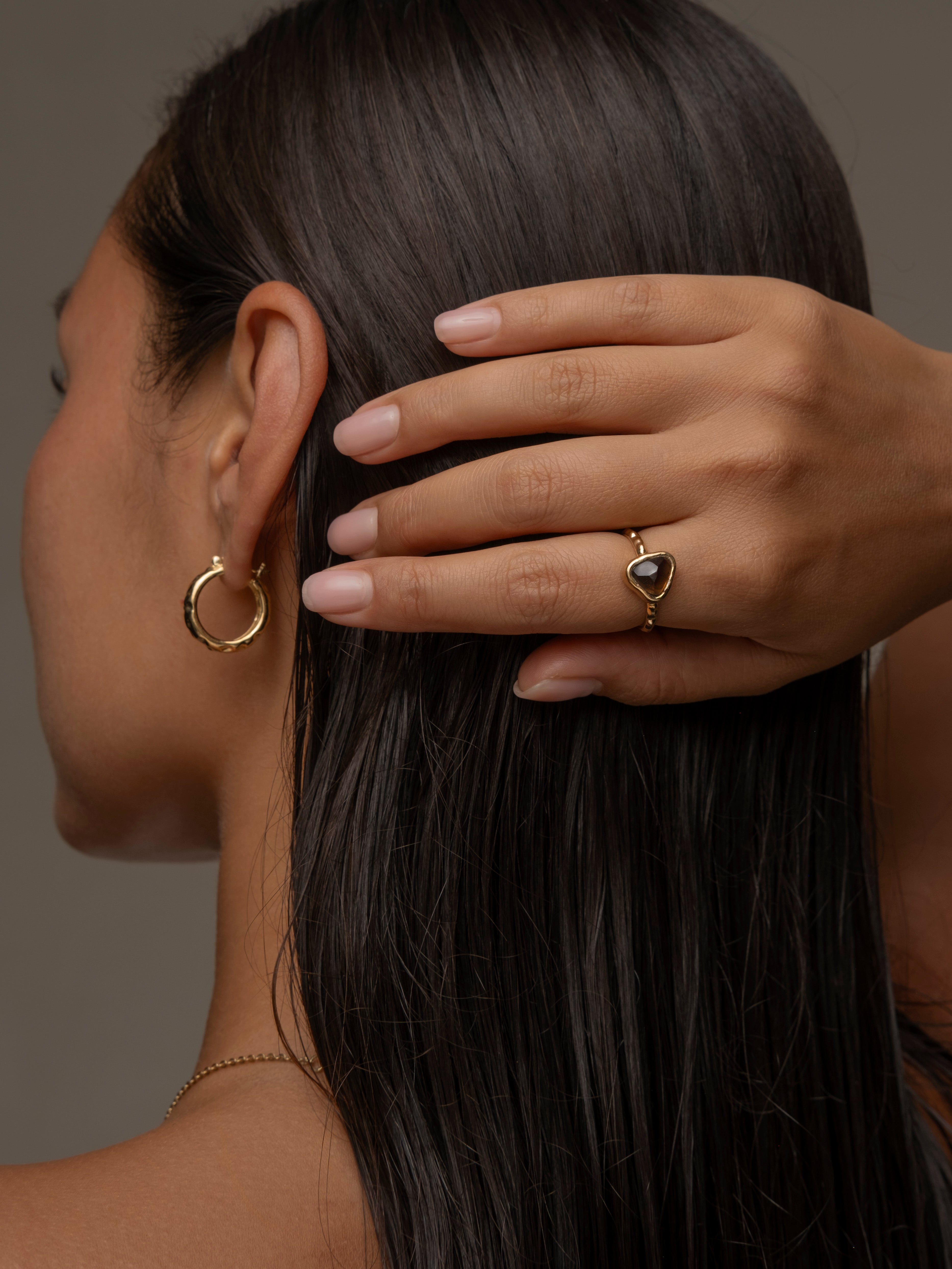 Woman wearing gold earring and ring with a triangular brown gemstone.