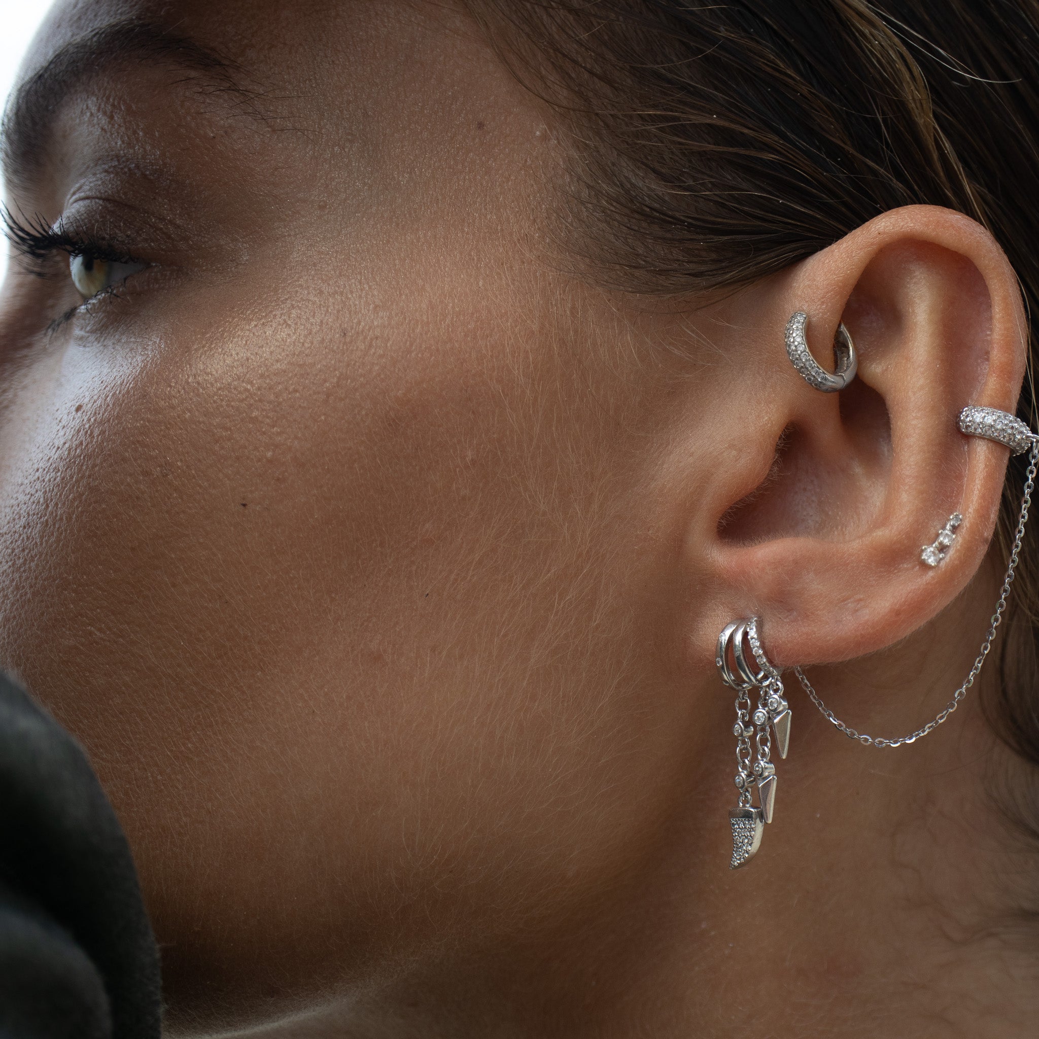 Close-up of woman wearing multiple earrings with chain.