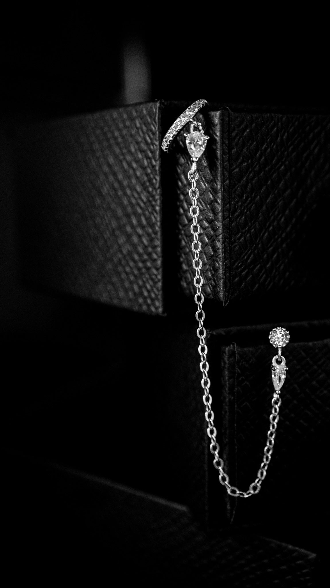 Silver chain earring with delicate design on black surface.