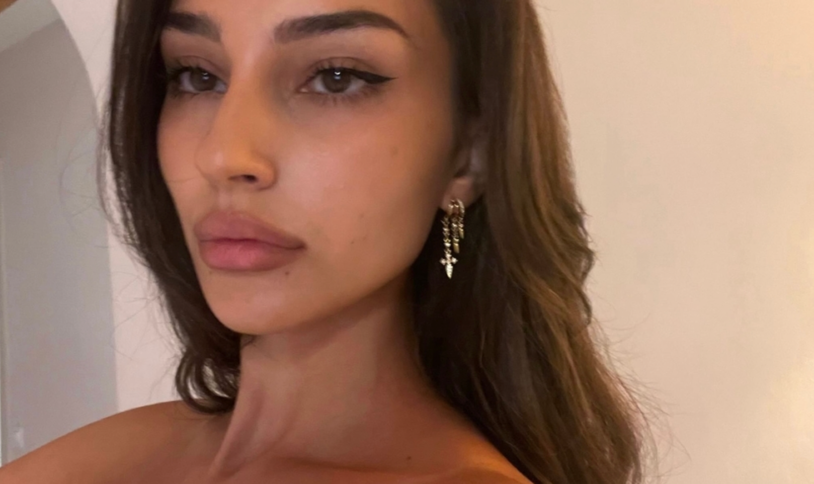 Close-up of a woman wearing Aaria London Angel Hoops earrings in gold, featuring elegant cross charms.