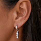 Close-up of ear with silver hoop and pointed drop earring.