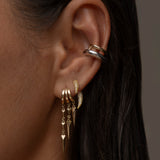 Close-up of a woman's ear adorned with multiple gold and silver earring, including dangling spikes.