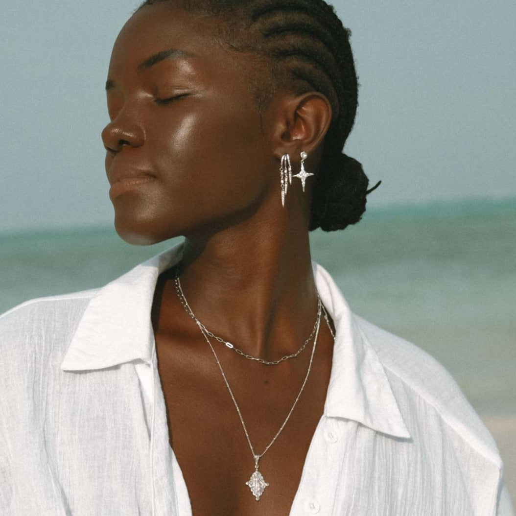 Close-up of woman wearing layered silver jewelry on a beach setting.