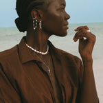 Woman wearing layered silver jewelry with chain earrings.