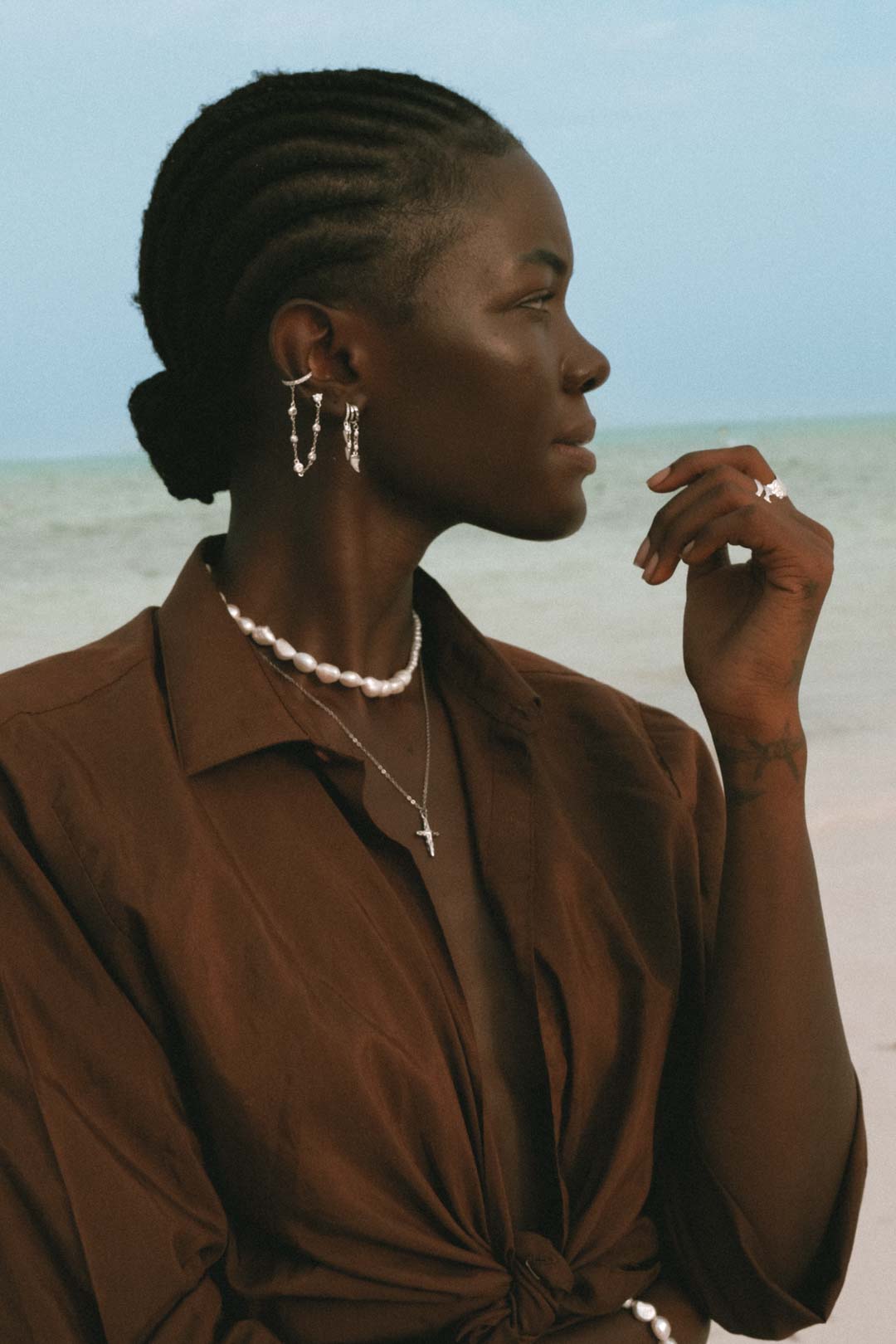 Woman wearing layered silver jewelry with chain earrings.