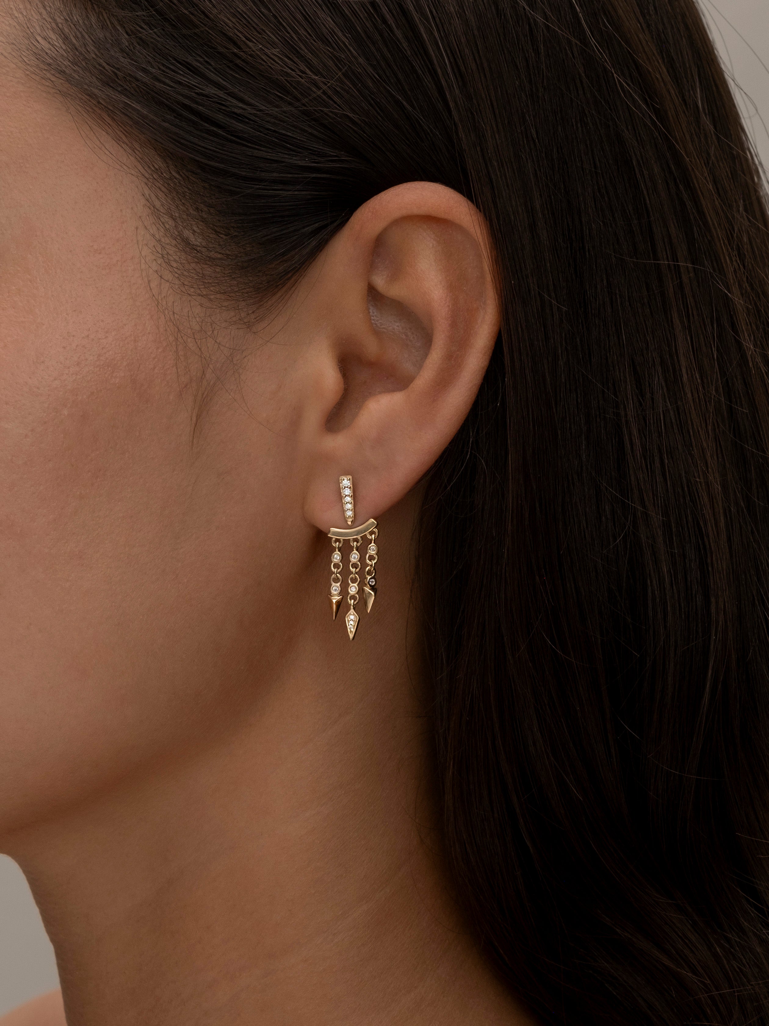 Close-up of woman's ear with gold dangling earrings.