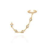 A gold ear cuff linked to a stud by a gemstone chain.
