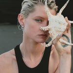 Stylish woman holding a seashell, wearing silver jewelry.