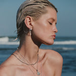 Model wearing layered silver necklaces and ear cuffs at beach.
