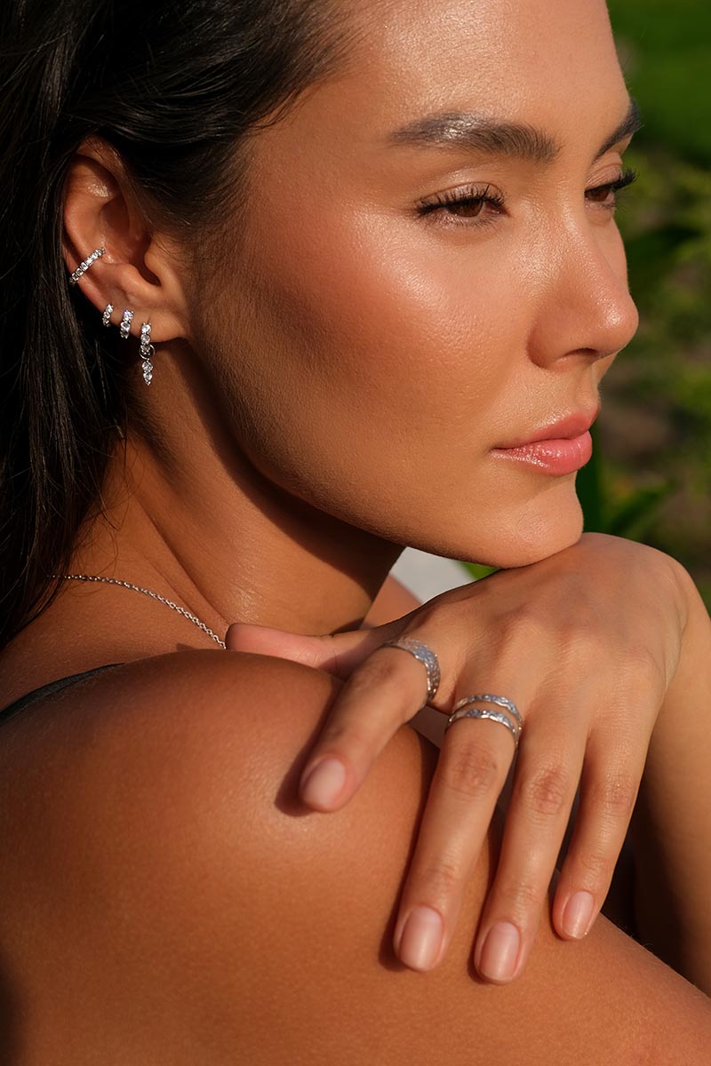 Portrait of a woman wearing diamond silver earrings, rings, and a silver necklace.