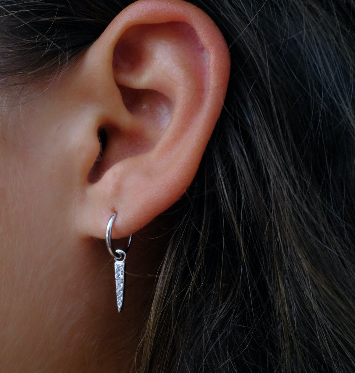 Close-up of ear with silver hoop & pointed drop earring. 