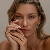 Woman with gold jewelry, including rings, necklace, and earrings.