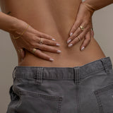 Hands on lower back adorned with gold rings and bracelets.