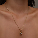 Woman wearing gold necklace with a triangular brown gemstone pendant.