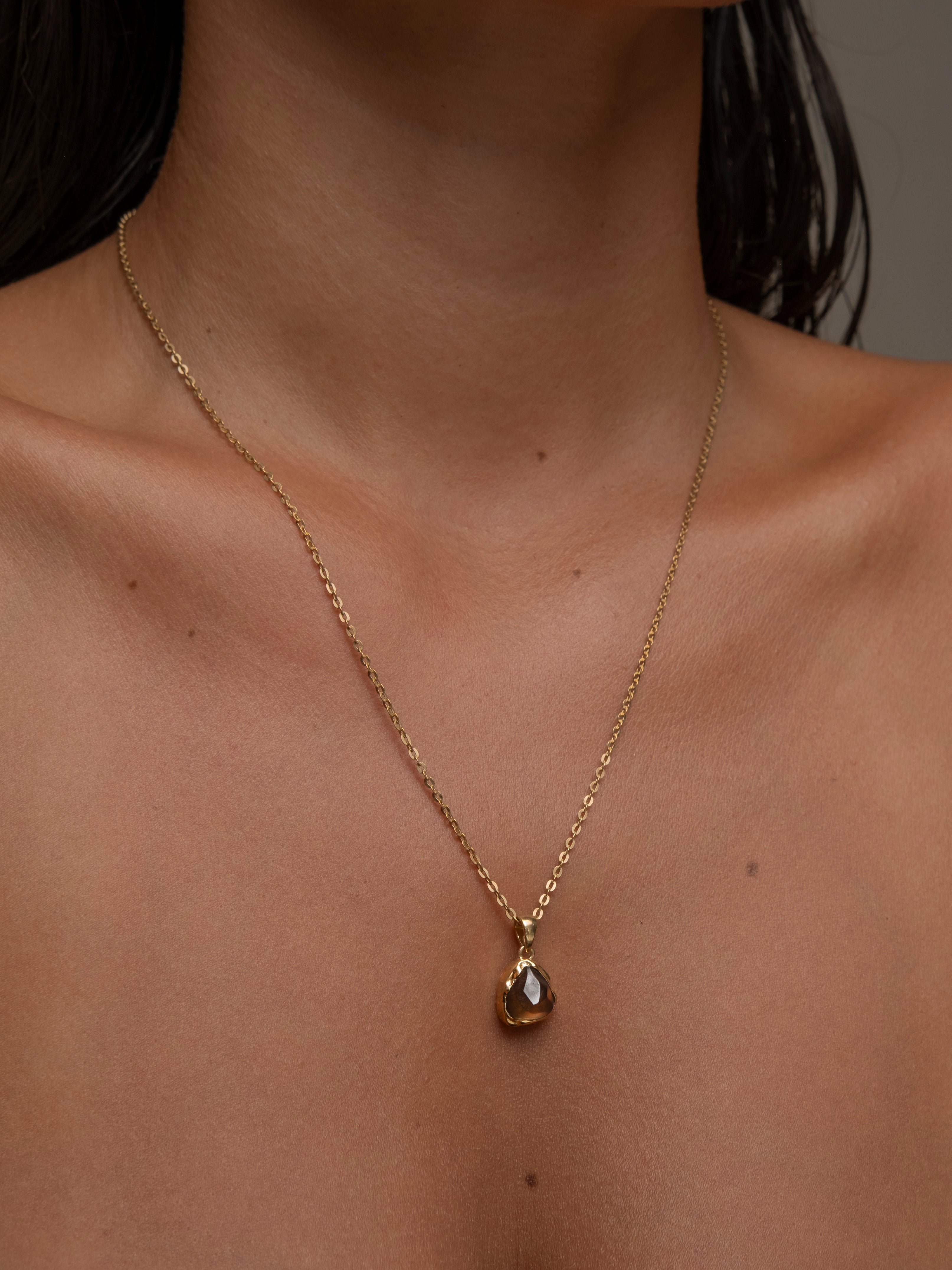 Woman wearing gold necklace with a triangular brown gemstone pendant.