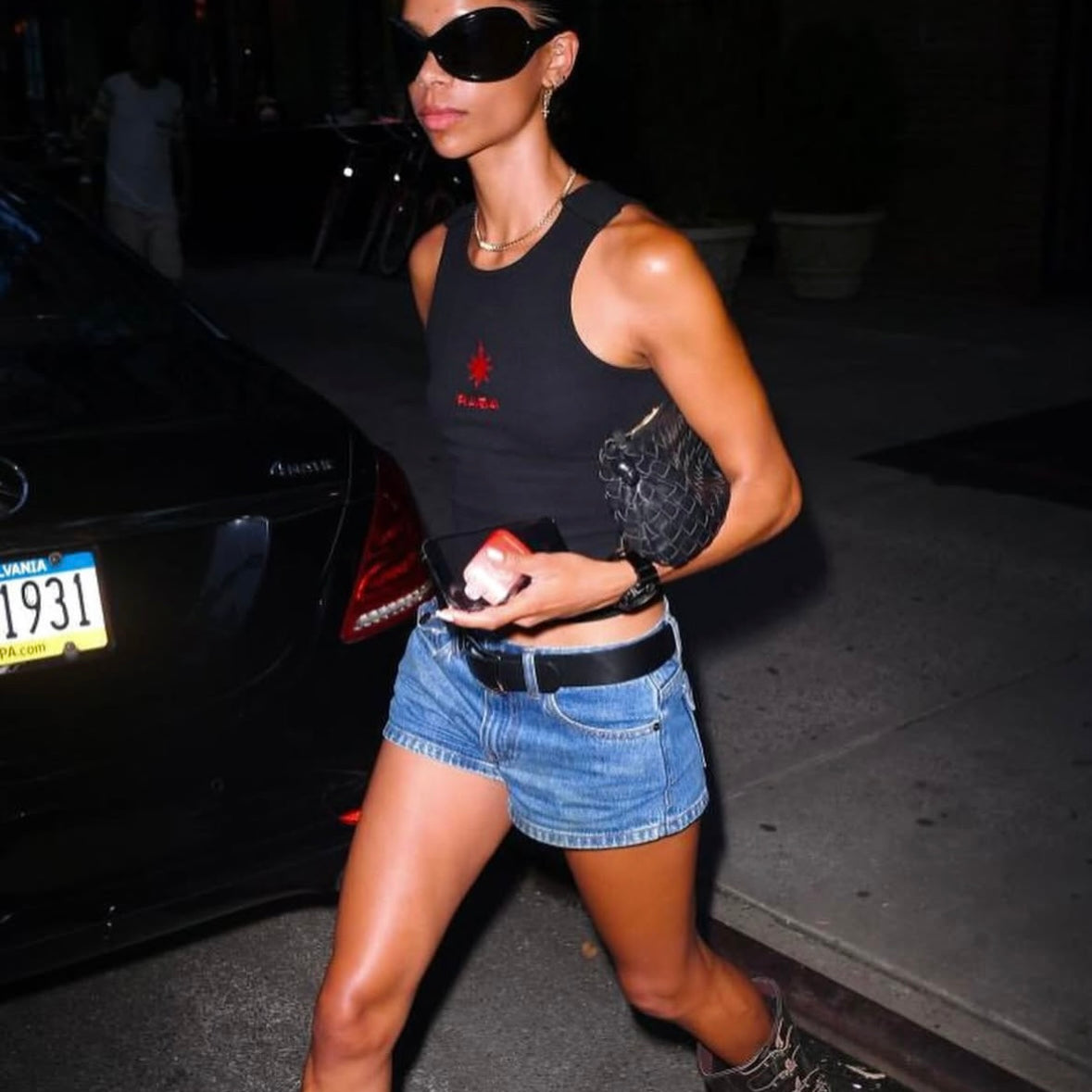 A stylish woman wearing denim shorts, a black crop top, oversized sunglasses, and Angel Hoops earrings.