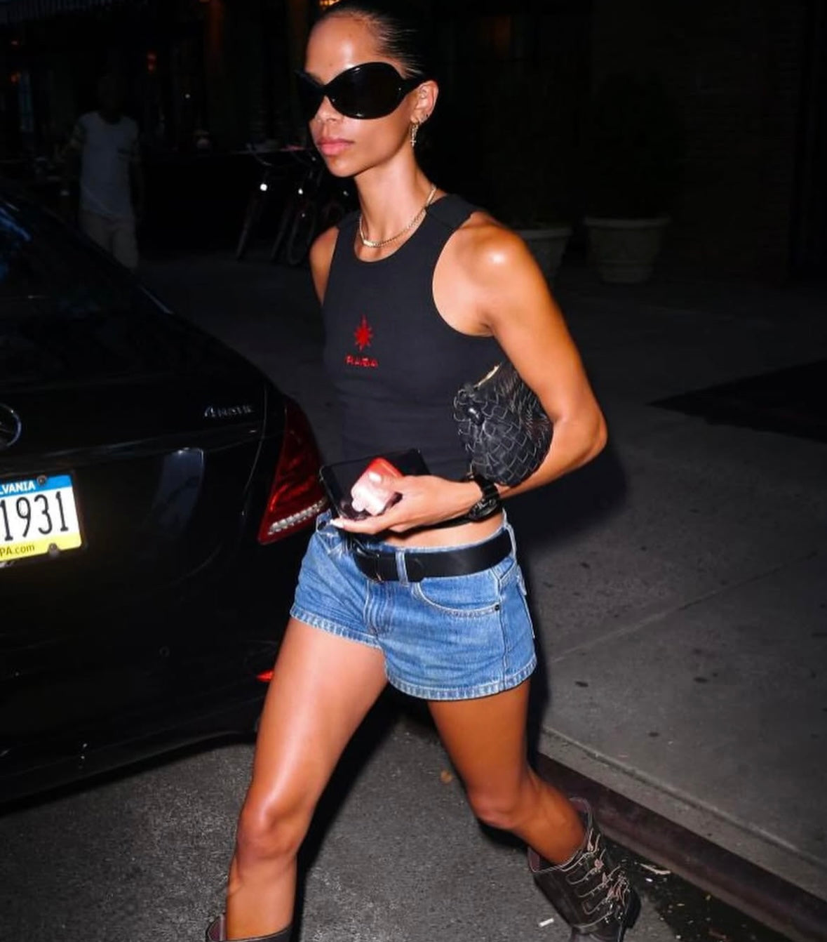 A stylish woman wearing denim shorts, a black crop top, oversized sunglasses, and Angel Hoops earrings.