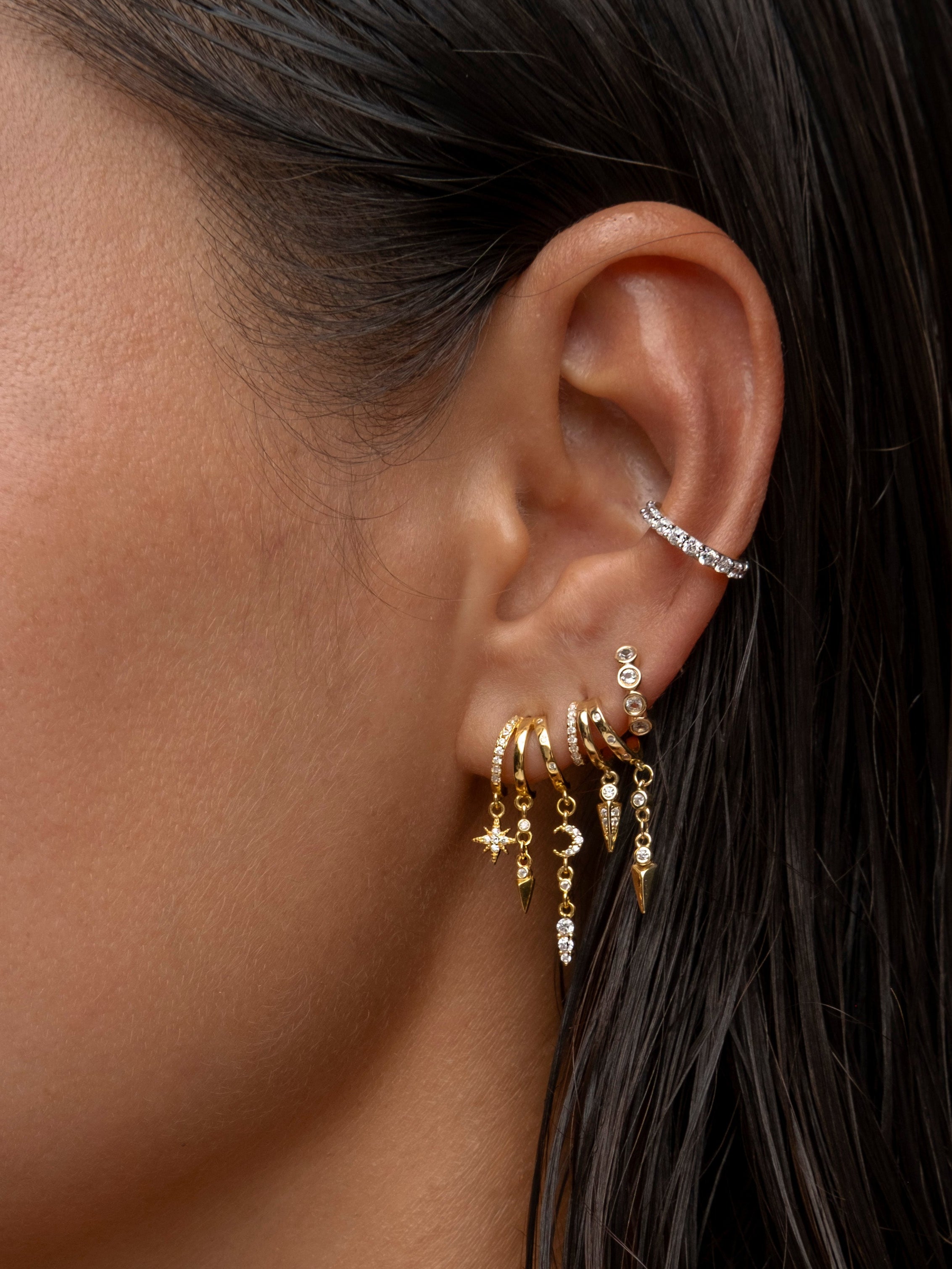 Gold and diamond dangling hoop earrings on a woman's ear.