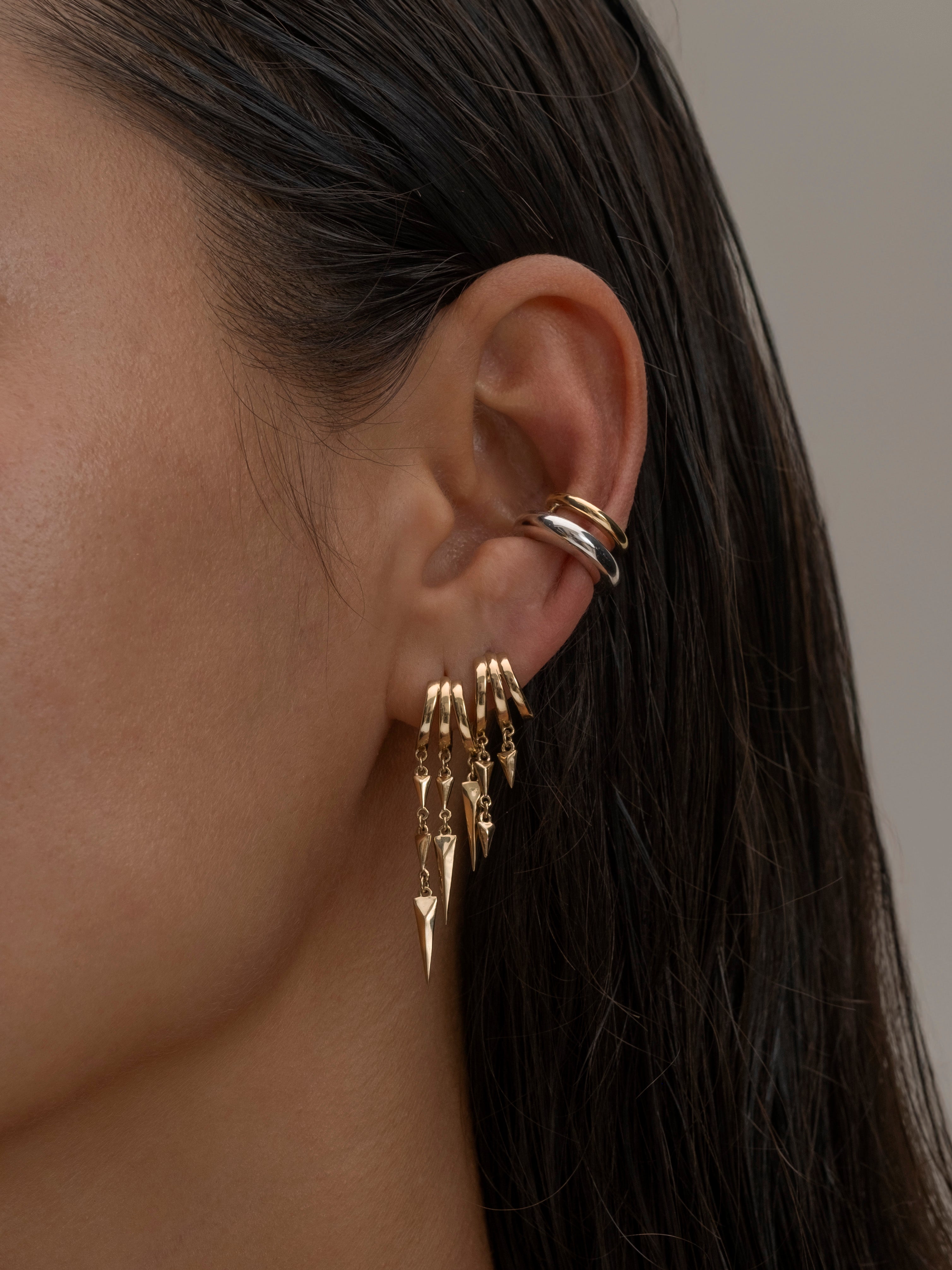 Close-up of a woman's ear adorned with multiple gold and silver earrings, including dangling spikes 4