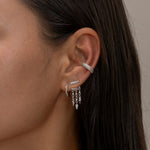 Silver ear cuff and dangling earrings on woman's ear.