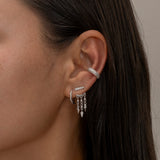 Silver ear cuff and dangling earrings on woman's ear.
