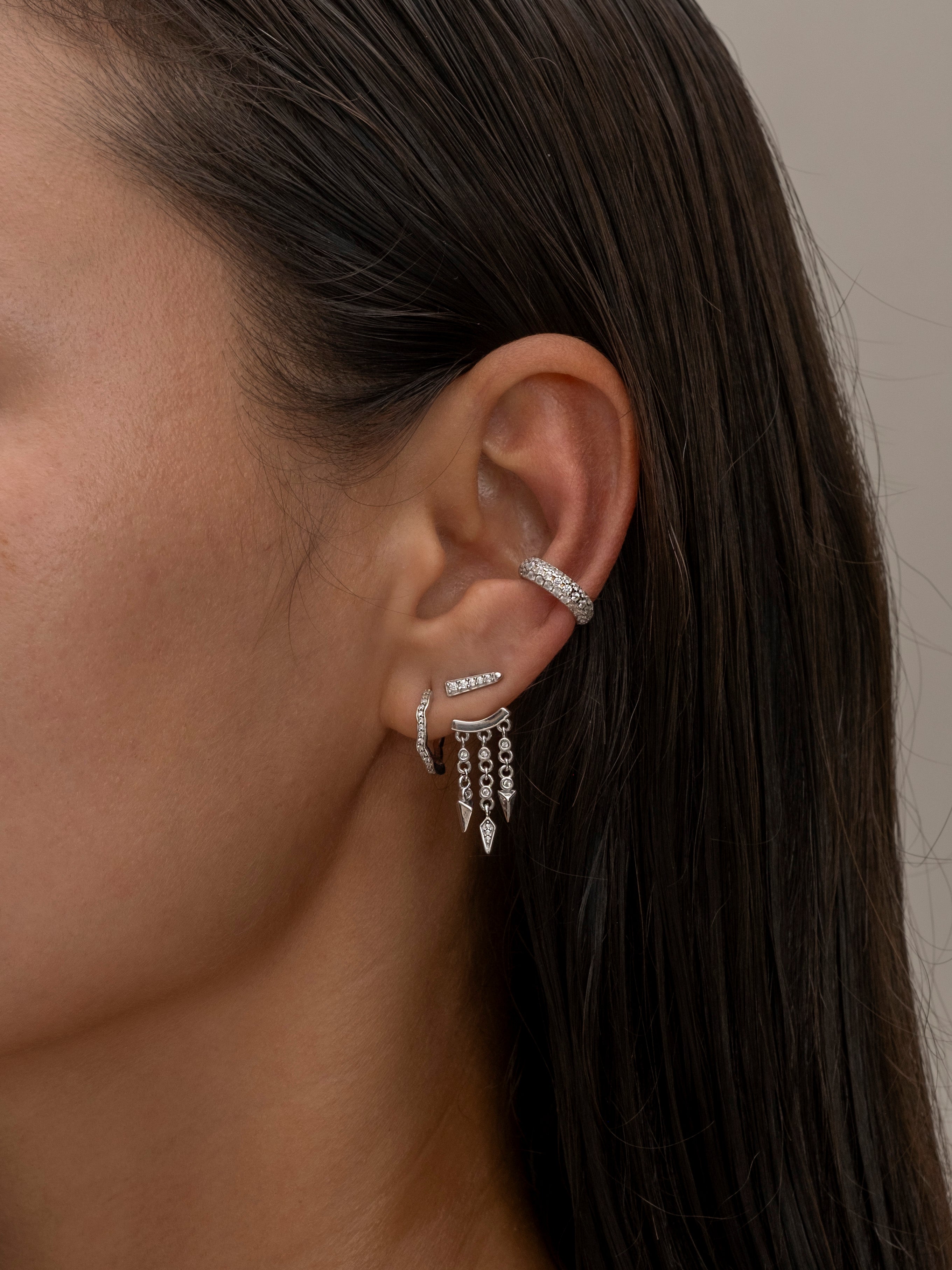 Silver ear cuff and dangling earrings on woman's ear.