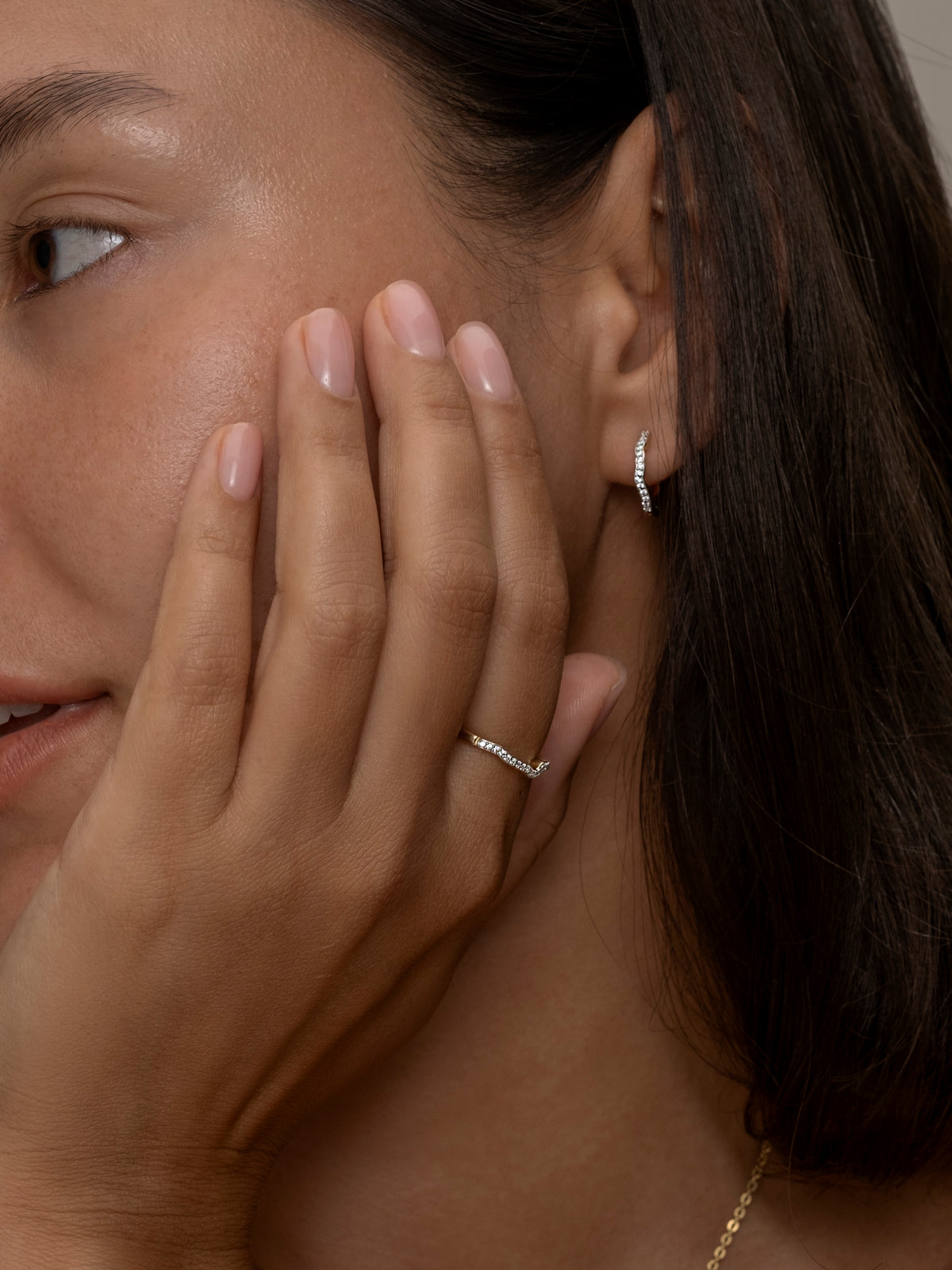 A women wearing delicate gold ring and earring with a subtle wavy diamond design. 
