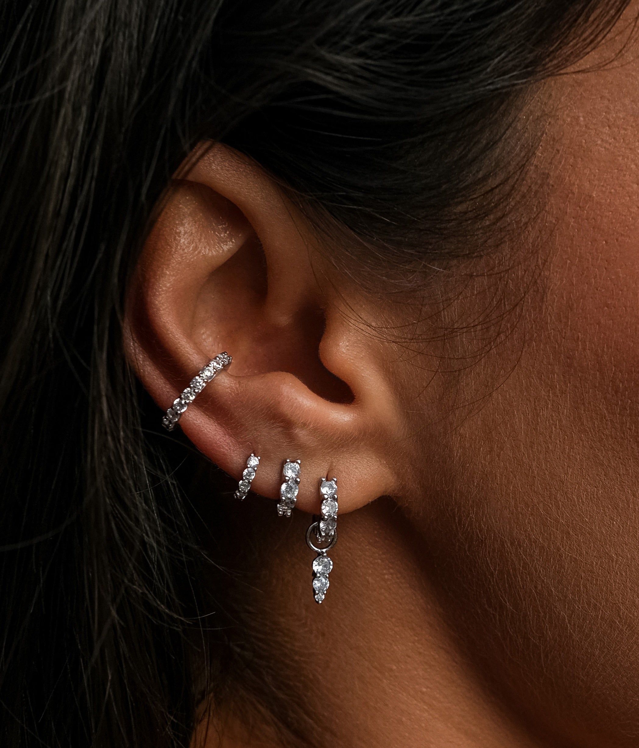 Close-up of a woman's ear adorned with multiple diamond earrings.