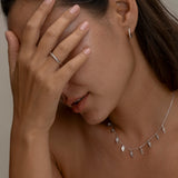 Woman covering face, wearing silver jewelry set.