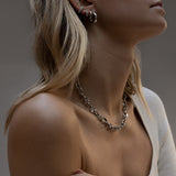 Woman wearing silver chunky chain necklace and hoop earrings.