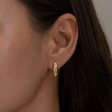 Small diamond-studded gold hoop earring on ear.