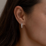 Small diamond-studded silver hoop earring on ear.
