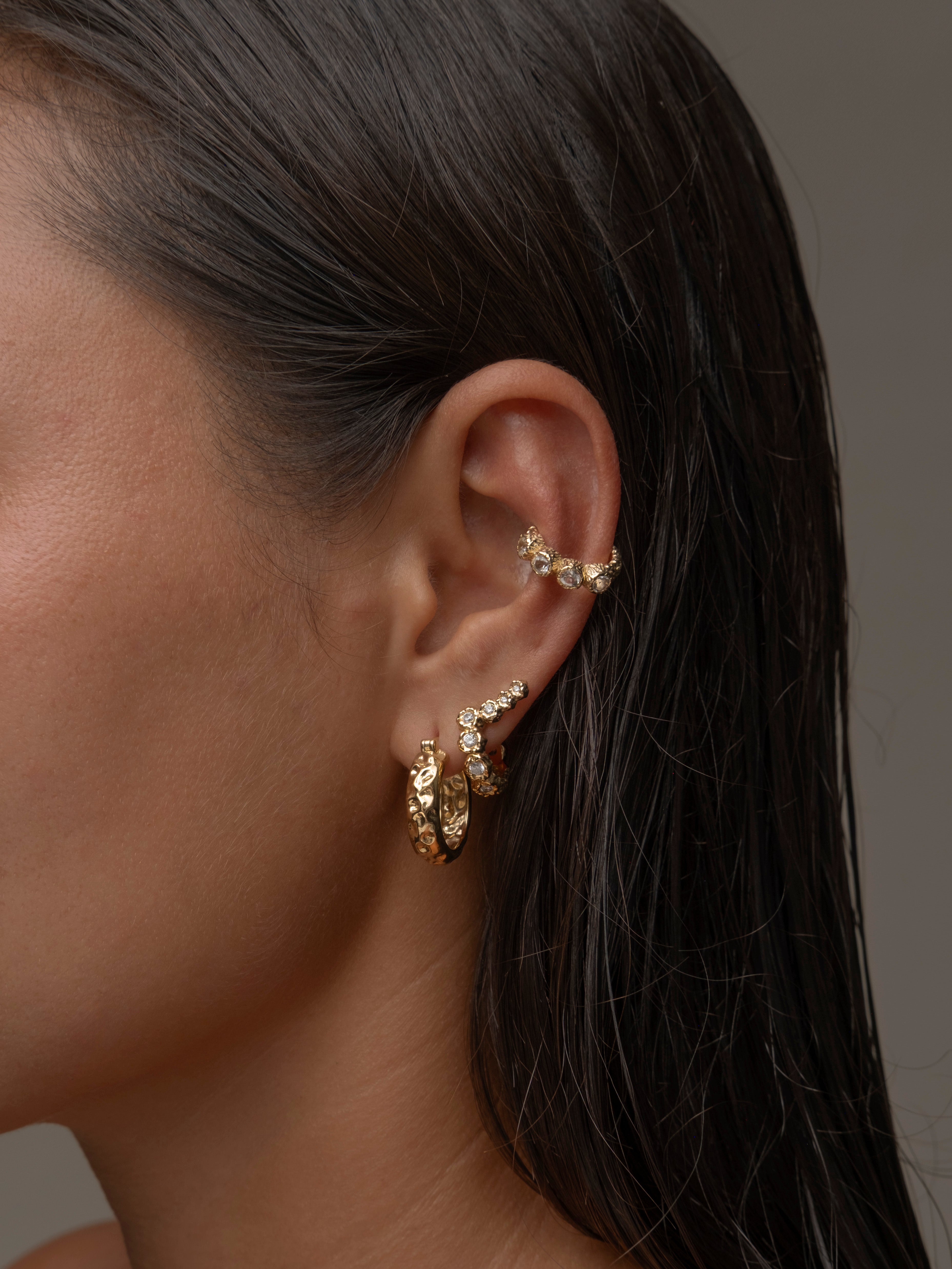 A woman's ear adorned with multiple gold earrings.