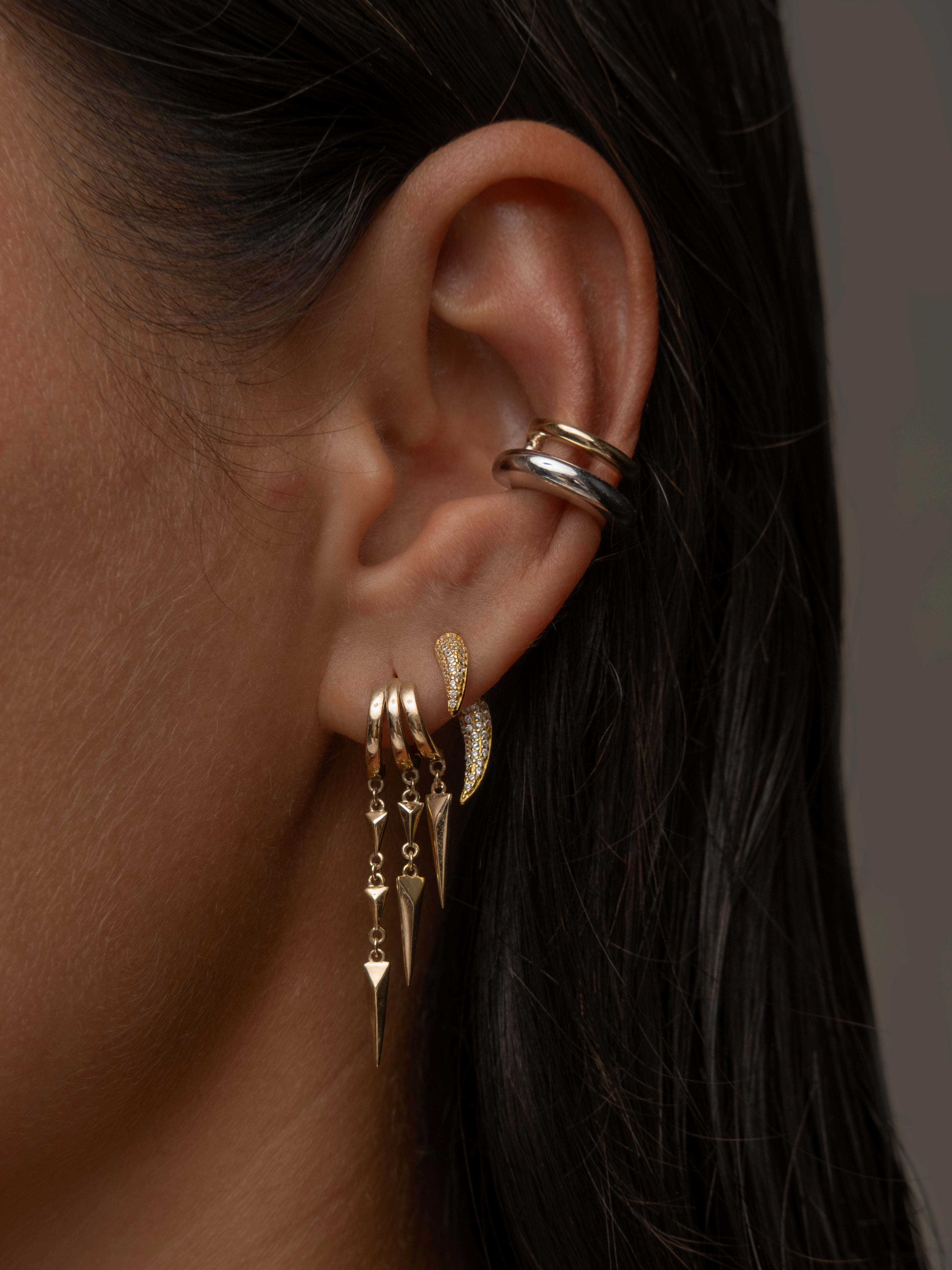 Close-up of a woman's ear adorned with multiple gold and silver earring, including dangling spikes.
