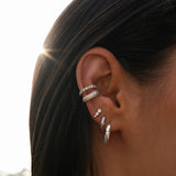 Close-up of a woman's ear adorned with multiple silver diamond earrings.