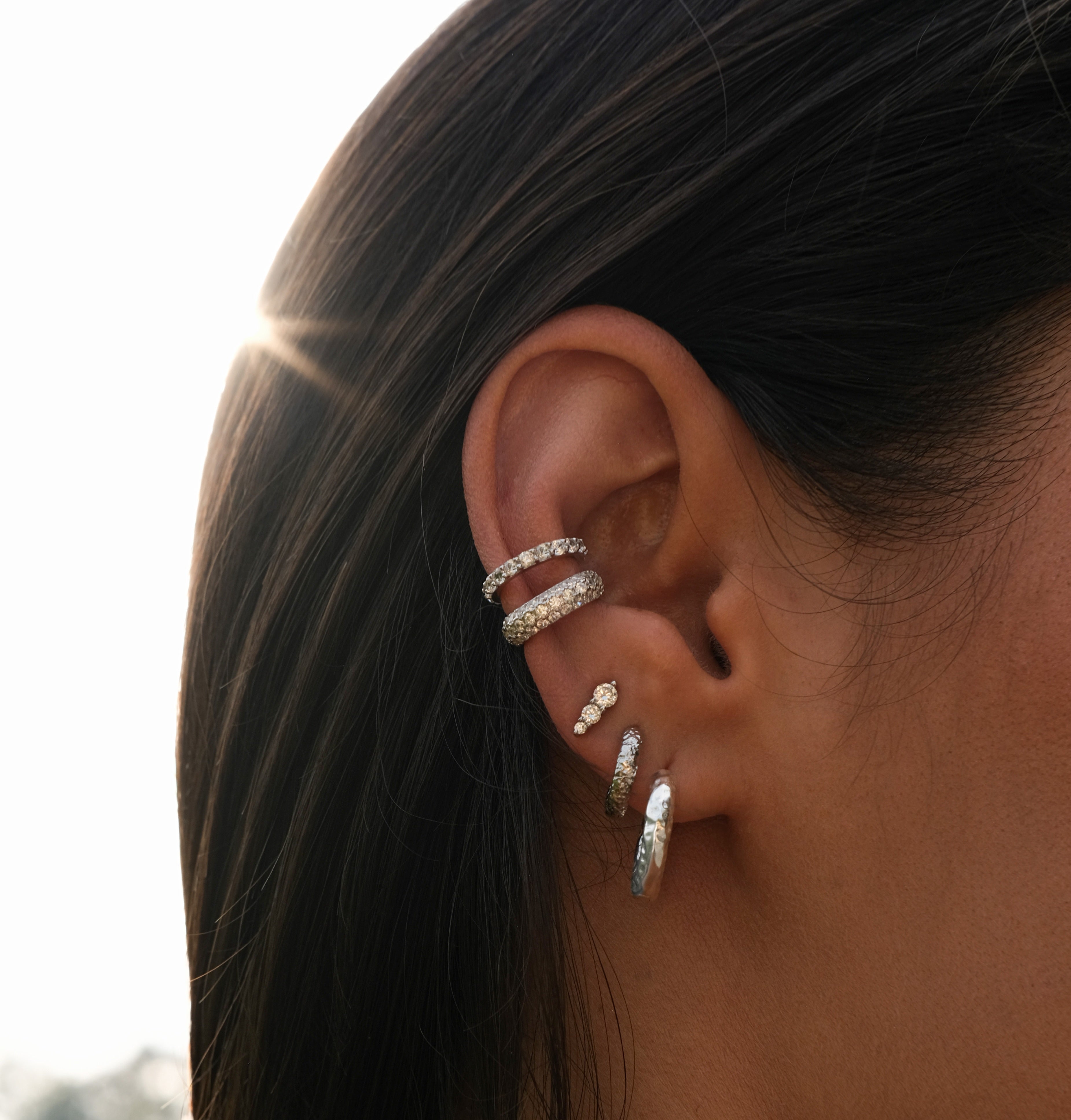 Close-up of a woman's ear adorned with multiple silver diamond earrings.